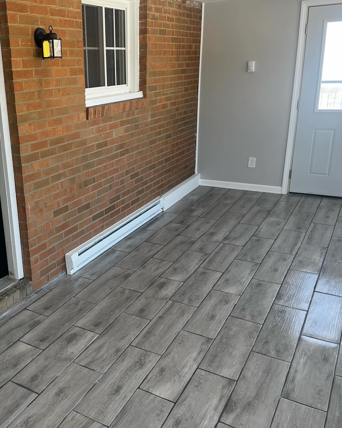 Gray wood-look tile flooring in entryway with brick wall