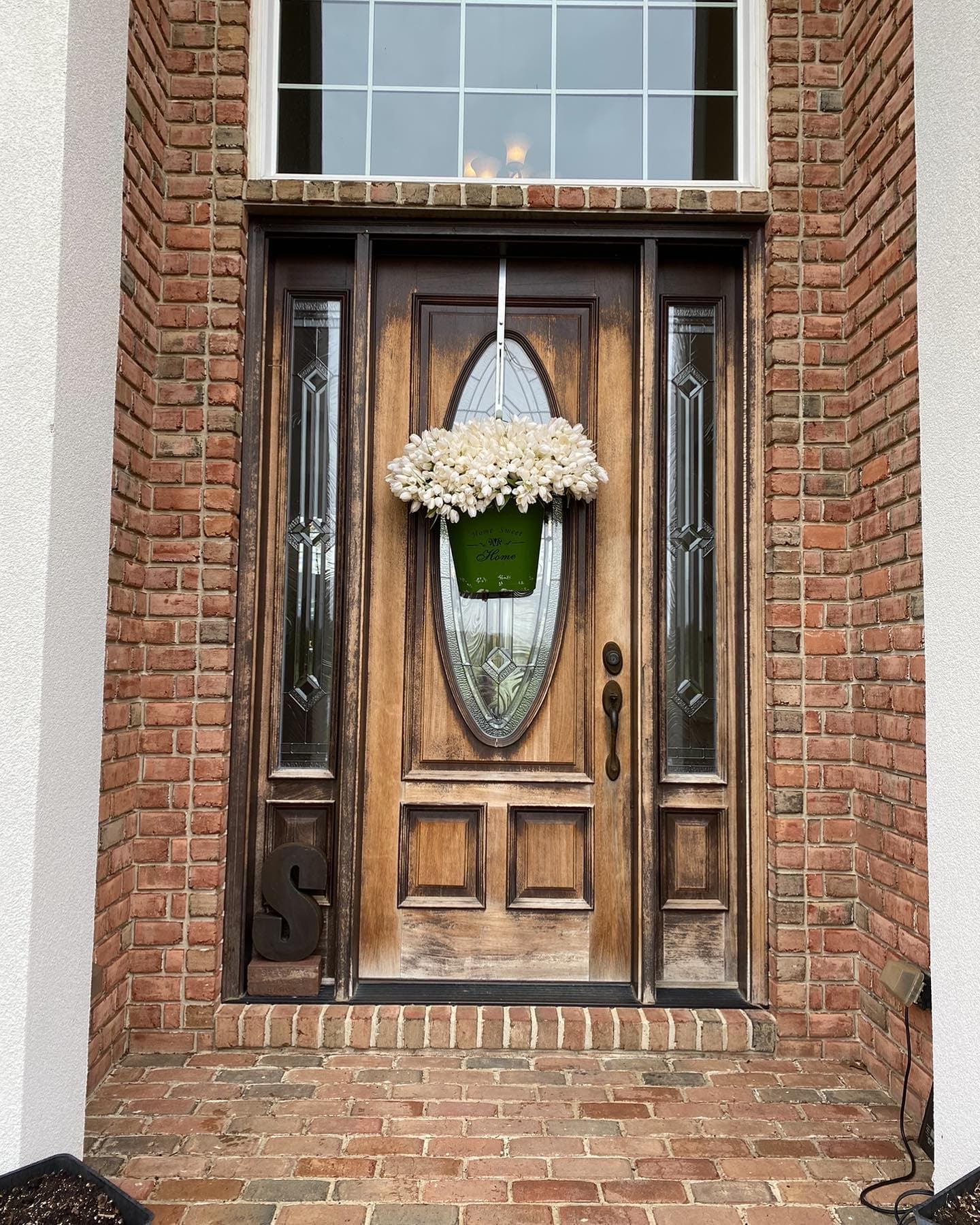 New wood-tone entry door with glass sidelights and brick surround