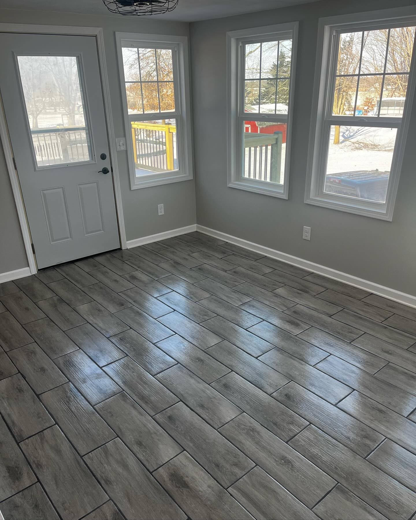 Gray tile flooring in sunroom with multiple windows and door