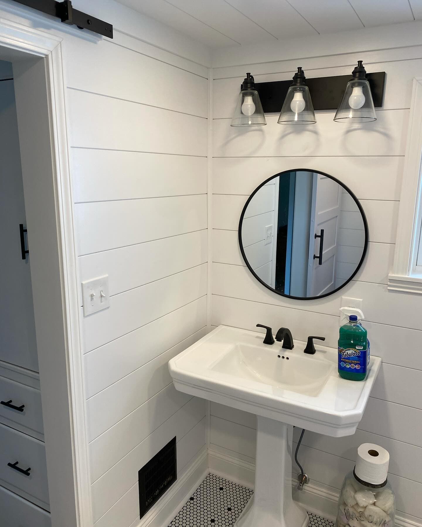 White shiplap bathroom with round mirror and pedestal sink
