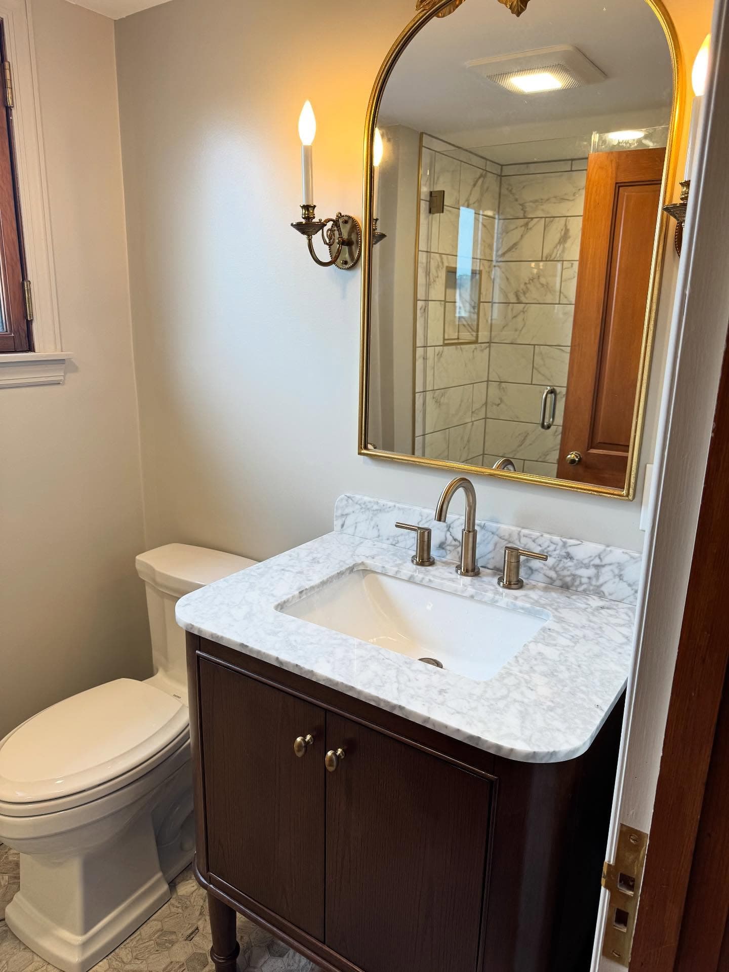 Marble tile shower reflected in gold arched mirror