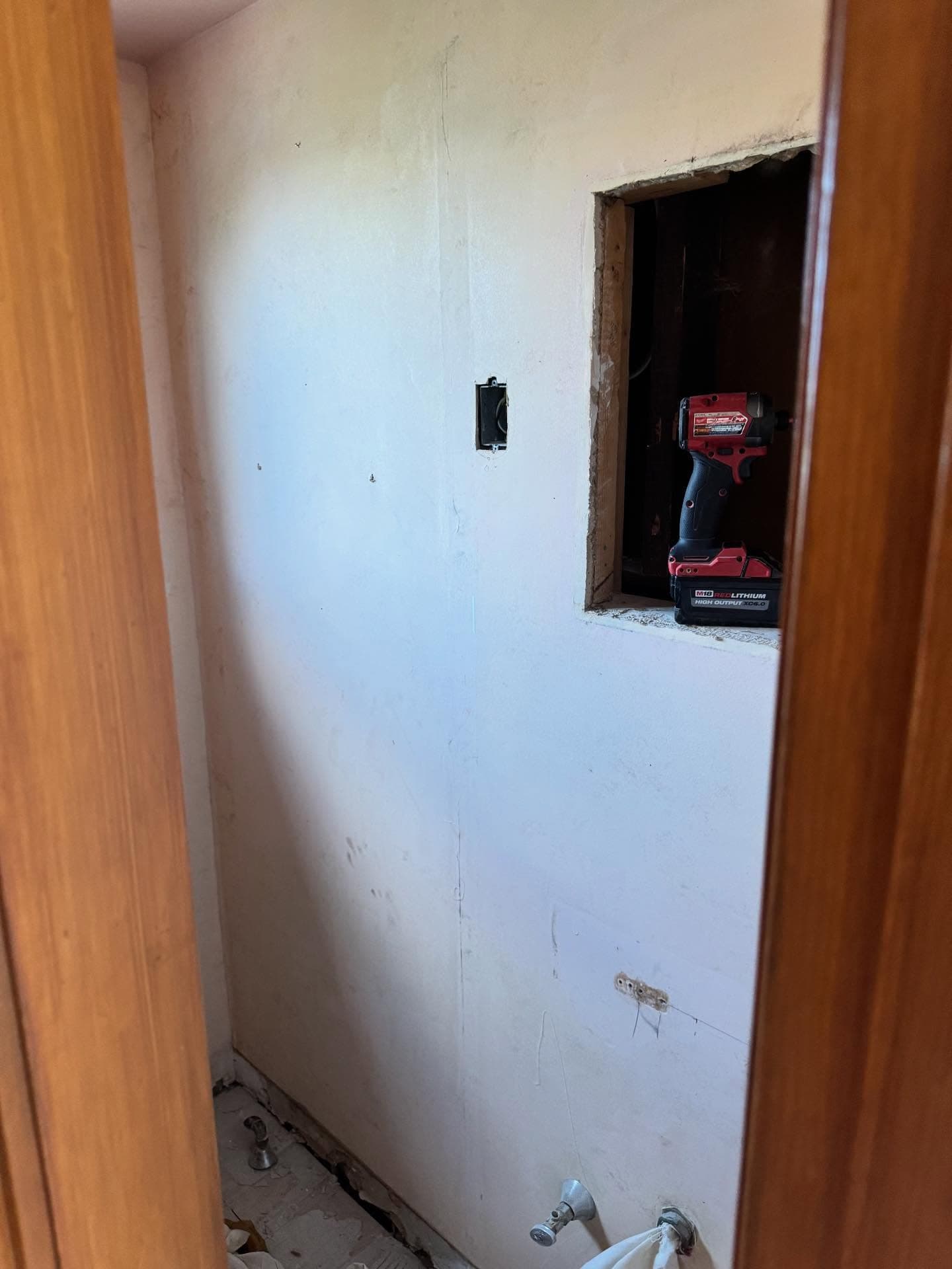 Wall repair in progress with an impact driver in an opened access panel
